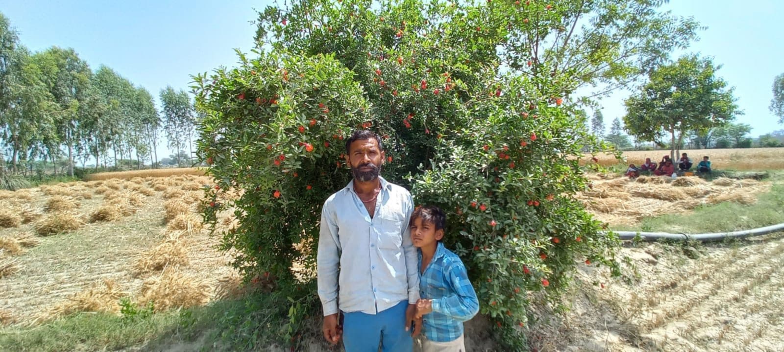 A farming couple beside the fruit tree they planted, during the 2022 post-plantation survey